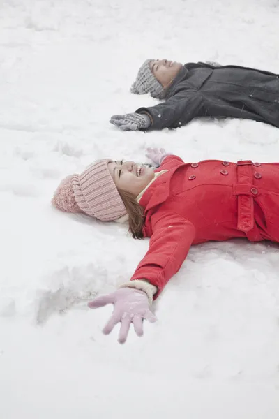 Coppia posa sulla neve facendo angeli della neve — Foto Stock