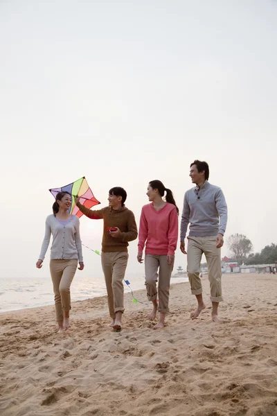 Jóvenes amigos volando una cometa en la playa — Foto de Stock