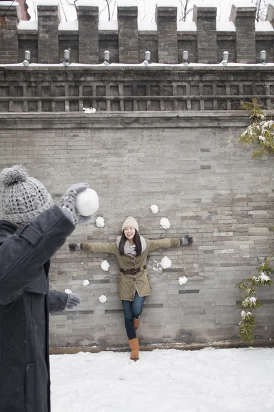 男人把雪球扔在墙上的年轻女子 — 图库照片