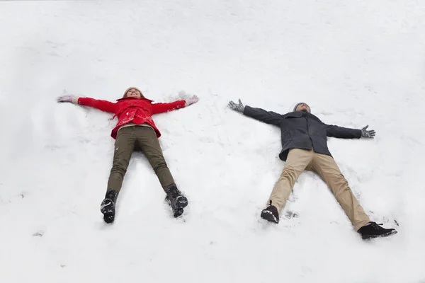 Pareja tendida en nieve haciendo ángeles de nieve —  Fotos de Stock