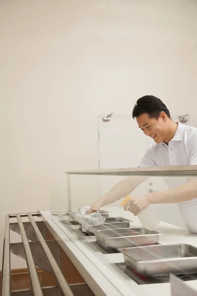 Cafeteria worker cleaning food serving area — Stock Photo, Image