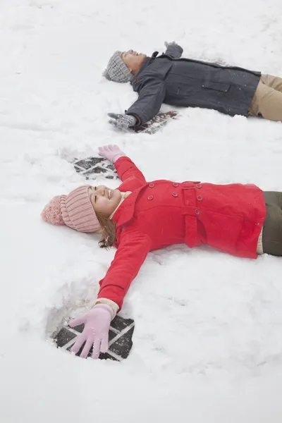 Coppia posa sulla neve facendo angeli della neve — Foto Stock