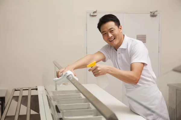 Cafeteria worker cleaning food serving area — Stock Photo, Image