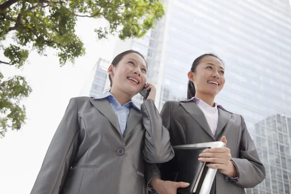 Duas jovens empresárias descendo a rua e conversando ao telefone — Fotografia de Stock