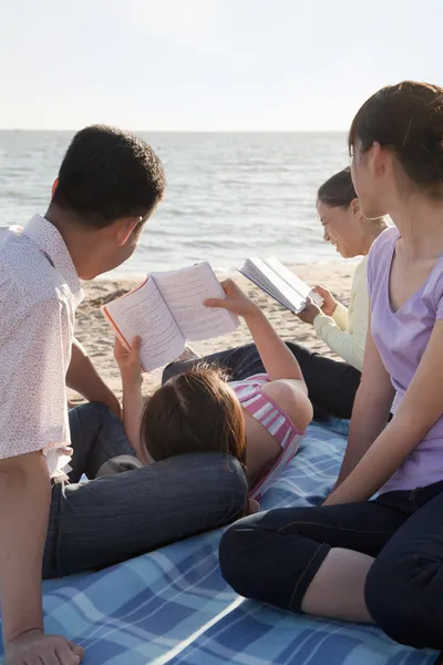 Multigenerational familj avkoppling och läsning på stranden — Stockfoto