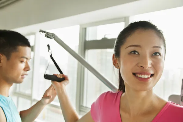 Mujer joven haciendo ejercicio con su entrenador personal en el gimnasio — Foto de Stock