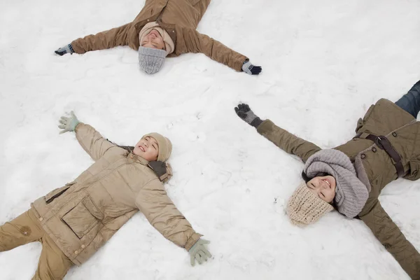 Família deitada na neve fazendo anjos de neve — Fotografia de Stock