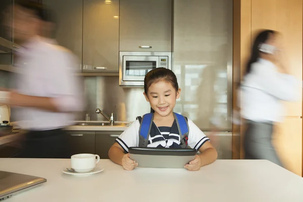 Daughter playing on digital tablet while parents running around — Stock Photo, Image