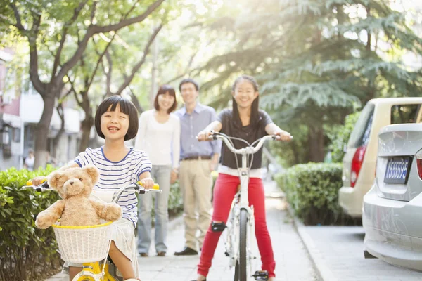 Hermanas montan en sus bicicletas mientras los padres observan —  Fotos de Stock