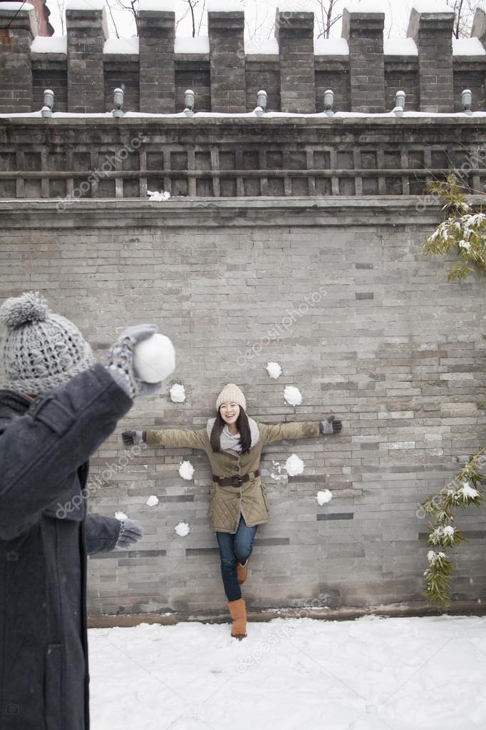 Man throwing snow balls at young woman on wall