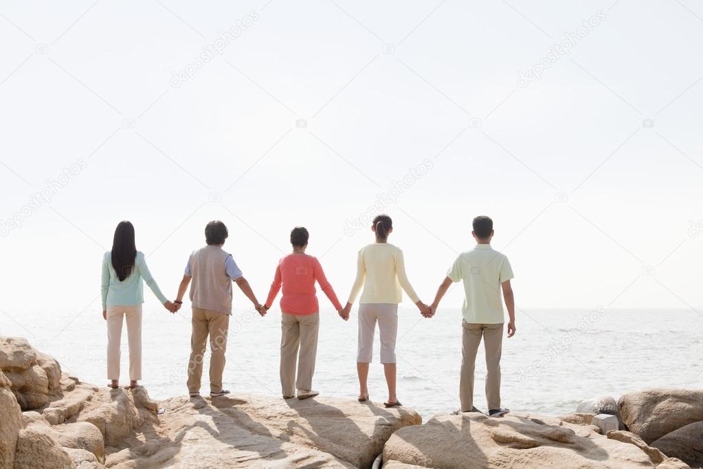 Multi-generational family holding hands on rocks by the sea