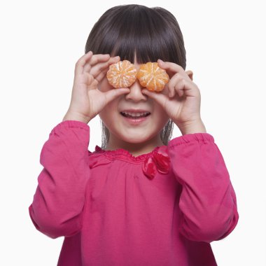 Little girl holding mandarins in front of her eyes clipart
