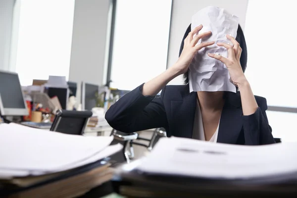 Businesswoman sitting at desk covering her face with a paper — Stock Photo, Image