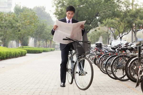 Businessman on a bicycle and reading the newspaper — Stock Photo, Image