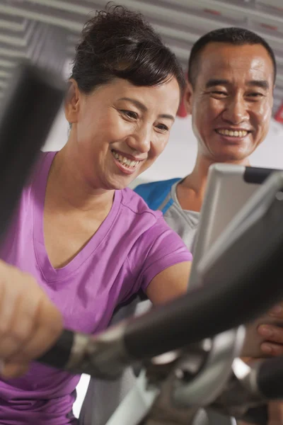 Woman exercising on the exercise bike with her trainer — Stock Photo, Image