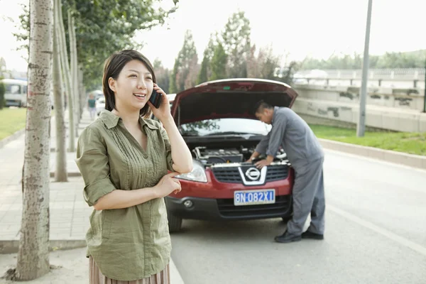 Frau telefoniert, während Mechaniker ihr Auto repariert — Stockfoto