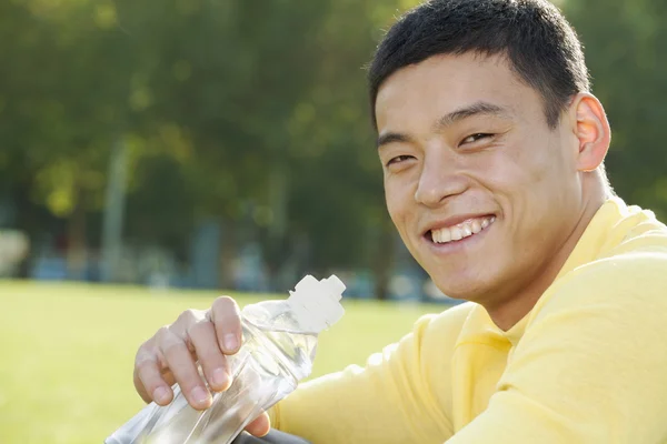 Sportlicher Mann sitzt auf dem Rasen in einem Park — Stockfoto