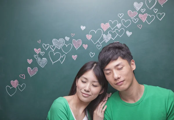 Couple in front of blackboard with hearts — Stock Photo, Image