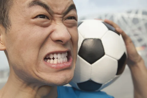 Joven enojado sosteniendo una pelota de fútbol — Foto de Stock