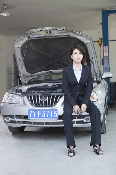 Geschäftsfrau sitzt auf Auto mit offener Motorhaube — Stockfoto