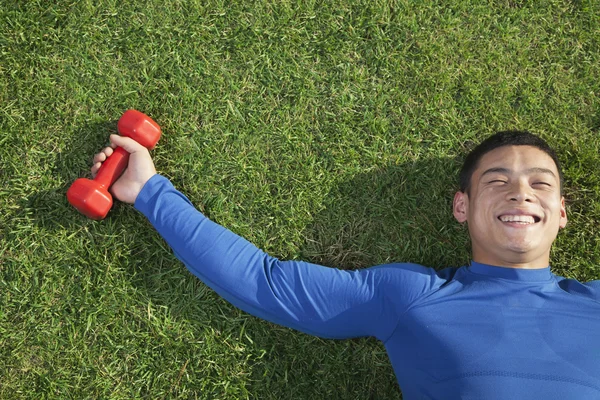 Athletic Man Lying Down in Grass with Dumbbells — Stock Photo, Image