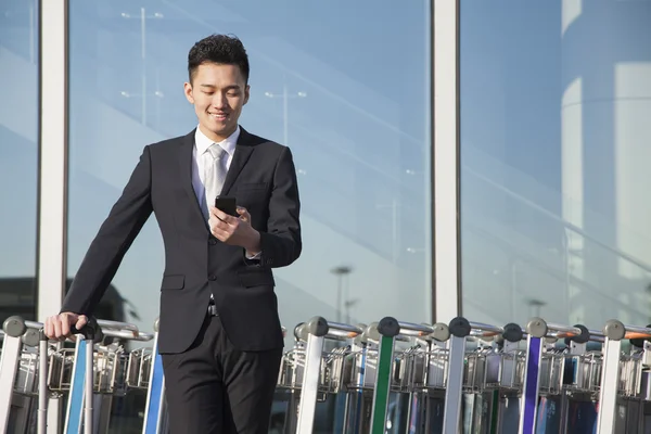 Traveler looking at cellphone next to row of luggage carts — Stock Photo, Image