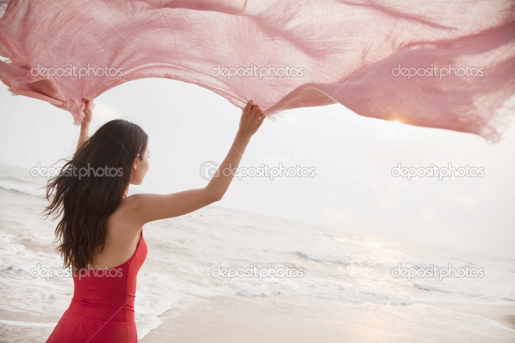 Woman on the beach holding scarf in the air