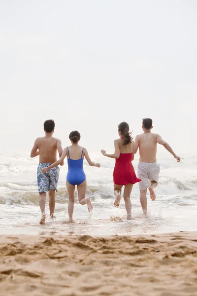 Друзья, бегущие в воду на песчаном пляже — стоковое фото