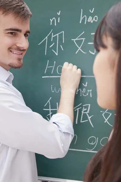Teacher with student in front of chalkboard writing — Stock Photo, Image
