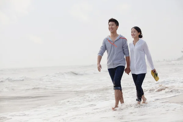Couple walking by the waters edge on the beach — Stock Photo, Image