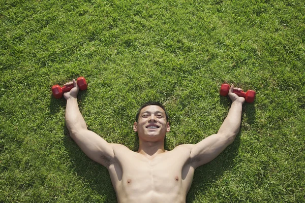 Homme couché dans l'herbe avec haltères — Photo