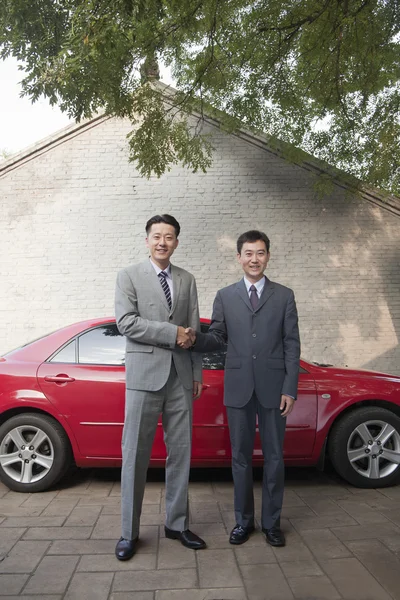 Два бизнесмена пожимают руки рядом с красной машиной — стоковое фото