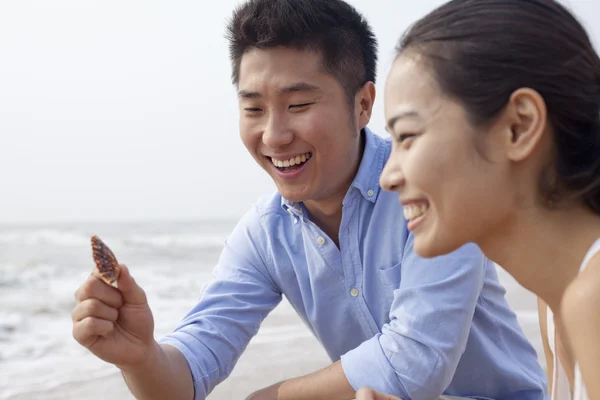 Couple looking at seashell at the waters edge — Stock Photo, Image