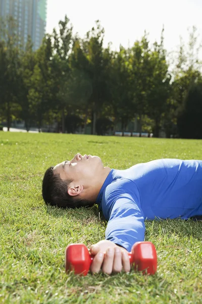 Athletic Man Lying Down in Park with Dumbbells — Stock Photo, Image