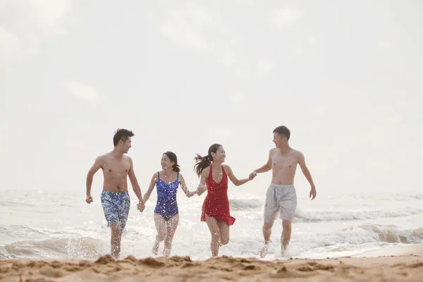 Amigos corriendo fuera del agua en una playa de arena —  Fotos de Stock