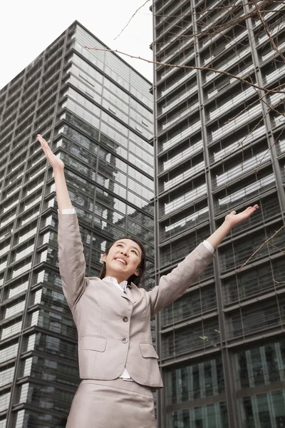 Businesswoman with arms outstretched among skyscrapers — Stock Photo, Image