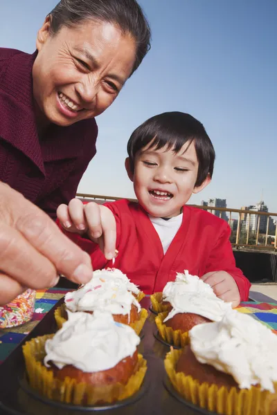 Grandmother and grandson decorating cupcakes — Stock Photo, Image