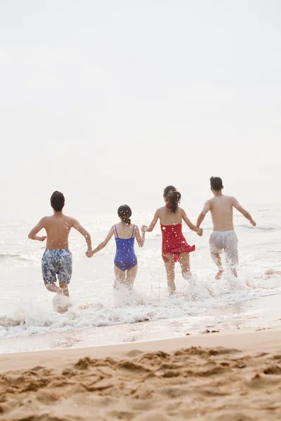 Friends running into the water on a sandy beach — Stock Photo, Image