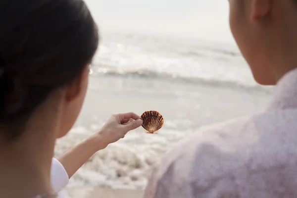 Pareja de pie y mirando la concha marina en la playa — Foto de Stock