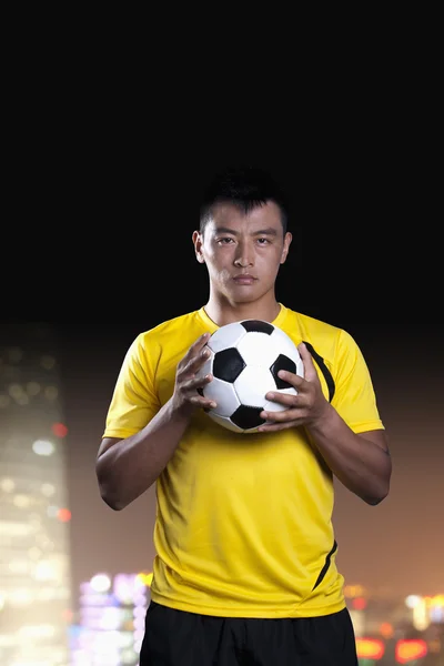 Giocatore che tiene un pallone da calcio, sfondo di notte — Foto Stock