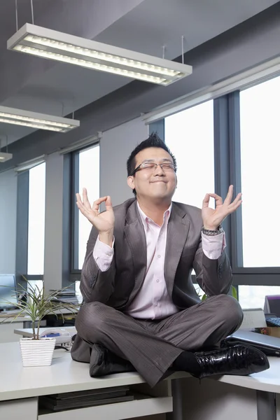 Businessman sitting on desk in the office meditating — Stock Photo, Image