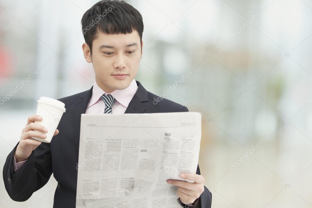 Business man holding coffee cup and reading newspaper
