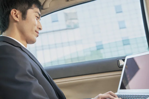 Empresario en asiento trasero del coche escribiendo en el ordenador portátil —  Fotos de Stock