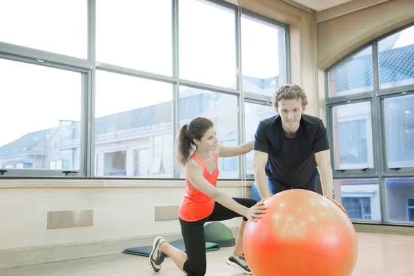 Fitness trainer helping young man with exercises — Stock Photo, Image