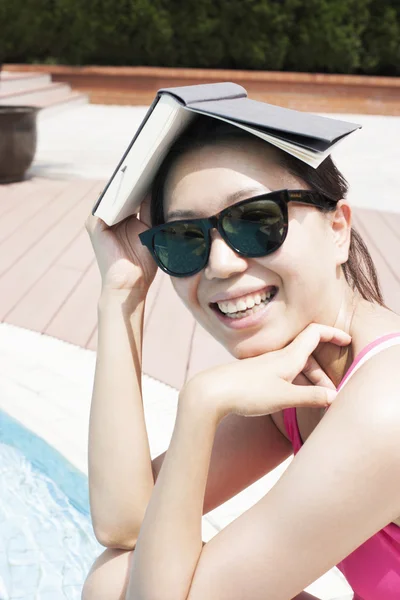 Kvinna vid poolen håller en bok över hennes huvud — Stockfoto