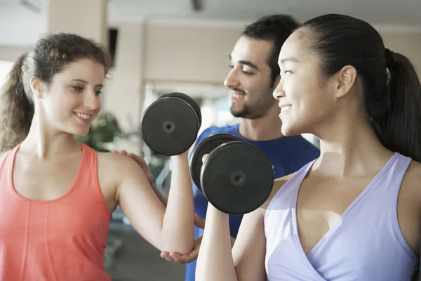 Fitness instructor helping two young women lift weights — Stock Photo, Image