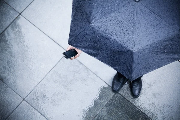 看着他的手机在雨中的商人 — 图库照片