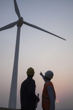 Günbatımında bir rüzgar türbini duran mühendisleri