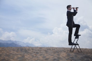 bir sandalye üzerinde duran ve teleskopla bakarak işadamı