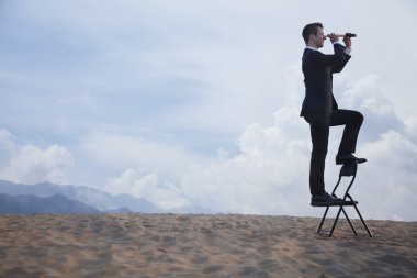 Businessman standing on a chair and looking through a telescope clipart